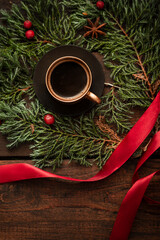 A small cup of espresso on a coniferous wreath with red berries.
