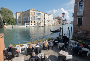 Tourists at the tables of a cafe on the Grand Canal near Rialto bridge Venezia, Italy