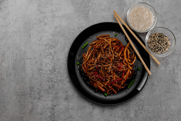 Spicy udon with chicken on a black plate and spices in glass bowls. View from above