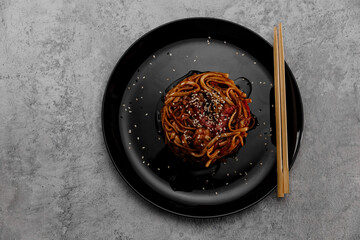 Spicy udon with chicken on a black plate on a gray cement background. View from above.