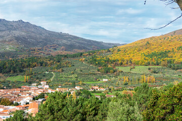 Paisaje de un pueblo montañoso español en otoño. Arboles en tonos naranjas y casas con paredes blancas 