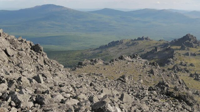 A woman climbs a mountain with a backpack. The tourist climbs to the top of the mountain. An aged woman travels. Ural mountains. Mount Silverstone.