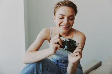 Woman photographer shooting in studio on old film camera at home on couch portrait, white...