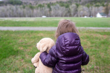 A little girl walks through a field with her stuffed animal doggie