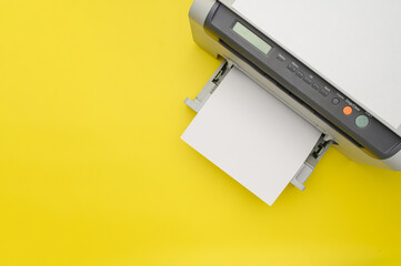 Top view of the printer and a blank sheet of a4 paper on a yellow background