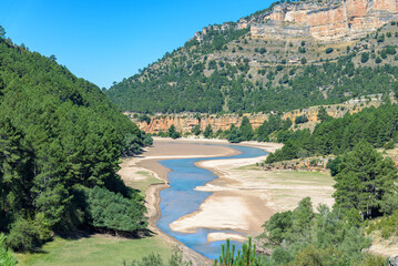 Beautiful landscape with a blue water river among the mountains and green forest on a cloudless day with blue sky, Cuenca mountain range Natural Park, Spain