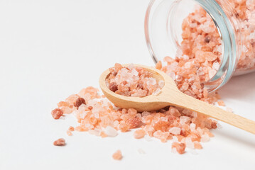 Fototapeta na wymiar Pink Himalayan coarse salt poured out of a glass jar and in wooden spoon on white background isolated