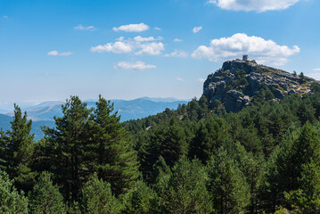 View of high mountains covered by green pine forest and a fire watch tower in the highest peak, Neila lagoons natural park at daylight, Neila, Burgos, Spain