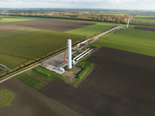 Building process of wind turbine windmill construction with cranes. Parts of the wind turbine, housing, hub, blades on site. Aerial drone overhead. Technical installation