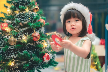 Asian little girl decorating Christmas tree at home, Merry Christmas Eve and Happy New Year concept.