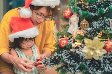 Happy asian mother and daughter decorating Christmas tree at home, Merry Christmas Eve and Happy New Year concept.