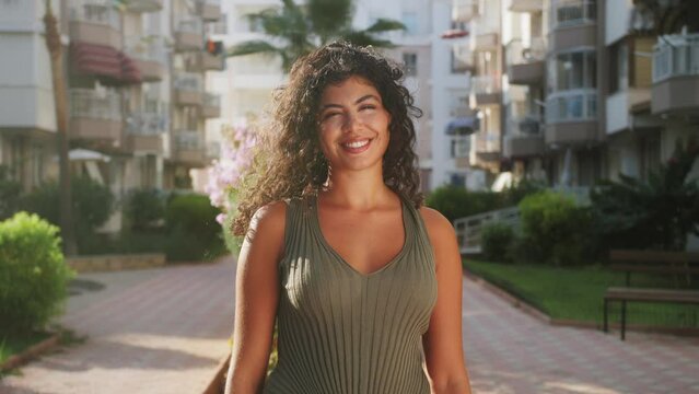 Curly carefree girl standing outdoor smiling looking at the camera. Happiness concept. Portrait of hispanic young woman.