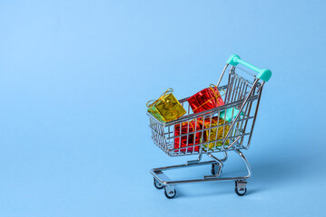 Close up of a small shopping cart full of colourful Christmas gifts on blue background. Copy space.