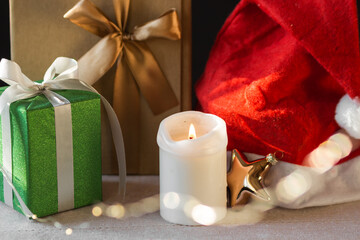 New Year or Christmas composition of wrapped gift boxes, burning candle and Santa's hat. Xmas garland bokeh light.