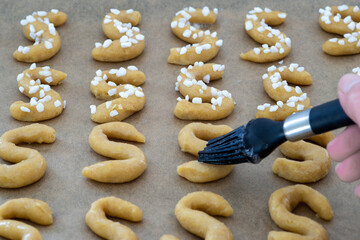 unbaked Christmas cookies on tray, woman hand with brush