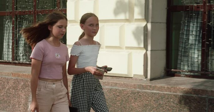 Teenage girls talking while walking by buildings. Tracking shot of female friends traveling in city. They are wearing casuals during summer weekend.