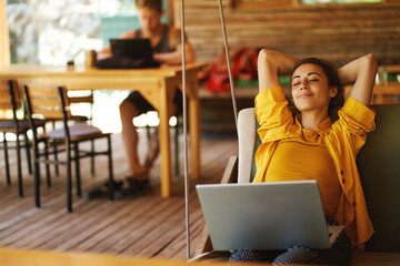 Carefree woman relaxing on swing in cafe shop or coworking hub with her laptop computer. Vacations and sometimes working remotely