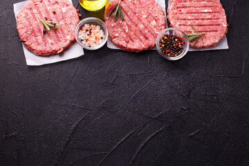 Raw fresh hamburger patties or cutlet ready to cook on black textured background. Minced beef steak burgers with spices. Top view. Place for text.