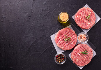 Minced beef steak burgers with spices. Raw fresh hamburger patties or cutlet ready to cook on black textured background.  Top view. Place for text.