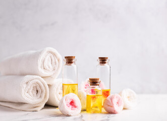 Fototapeta na wymiar Spa setting. Bottles with rose essential aroma oil, rose flowers and white towels on light grey textured background. Selective focus. Place for text.