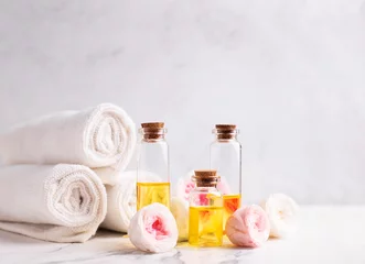 Spa-Einstellung. Flaschen mit ätherischem Rosenaromaöl, Rosenblüten und weißen Handtüchern auf hellgrauem, strukturiertem Hintergrund. Selektiver Fokus. Platz für Text. © daffodilred