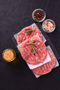 Raw fresh hamburger patties or cutlet ready to cook on black textured background. Minced beef steak burgers with spices. Top view.