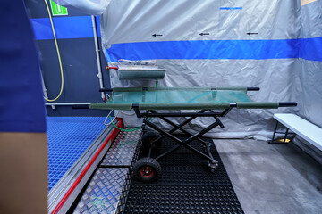 Interior of mobile plastic decontamination shower tent with small steel wash basin, mobile stretcher near