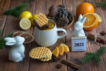 Calendar for 2023 and fragrant tea with orange and spices on a wooden table. Pie, lemons, oranges winter mood.