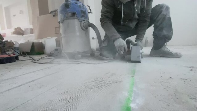 A man makes recesses in the concrete floor for installing underfloor heating with a wall chaser 