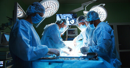 Team of professional mixed-races doctors and assistants in medical uniforms performs heart...
