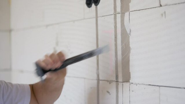 Construction worker expanding electric cable chase grooves with wall chisel, detail on hands holding the tool and hitting hammer