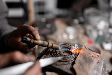 A craftsman jeweler is heating a piece of metal with a blowtorch to create a jewel