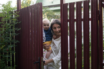 Obraz premium Curious woman with a baby peeps openint the gate of fence