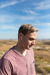 A man listens to music with headphones while thinking or meditating on a walk in the countryside and nature