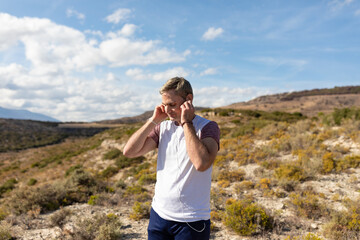 A man puts on headphones to listen to music before beginning a session of exercise and sport in the countryside and nature