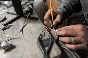 A craftsman jeweler is using a pencil to mark a piece of metal to create a jewel
