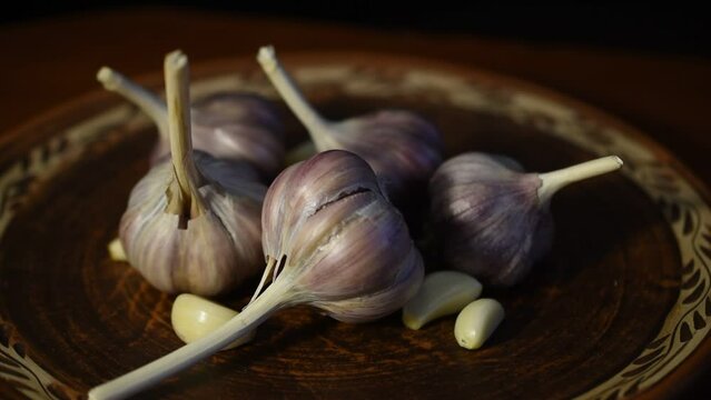 There are several heads of sharp, fragrant garlic on a clay plate. The plate is rotating.
