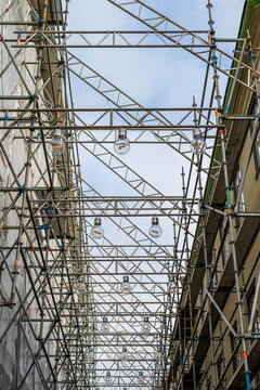 Scaffolding over a narrow street with lanps hanging underneath.