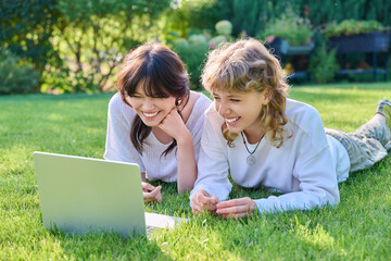 Fototapeta premium Teenage female student friends laughing lying on grass with laptop