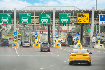 View with cars at the entrance or exit to a toll road limited by a barrier. Cashless payment transponder barrier, speed limit signs.
