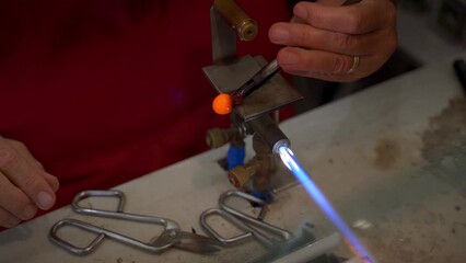 Murano glass blowing factory. Workers put iron rod in furnace to make glass malleable.
Artist shaping hot glass into a figurine with gas flames. Artisan making glass vases and sculptures. Venice.