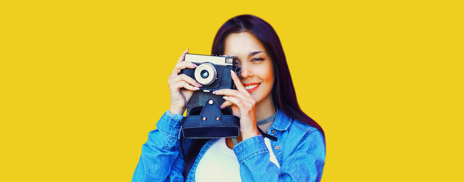 Portrait of young woman photographer with vintage film camera on yellow background