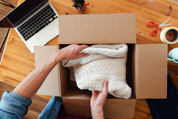 Top down view of man packing clothes into cardboard boxes to send it to client 