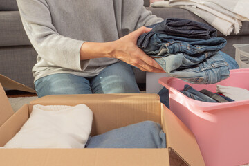 Obraz premium Woman sorting clothes and packing into cardboard box. Donations for charity, help low income families, declutter home, sell online, moving moving into new home, recycling, sustainable living concept