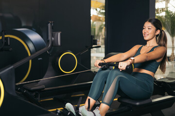 Fototapeta na wymiar A young Asian girl doing cardio exercise on an electric rowing machine,gym.