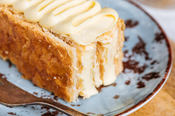 French dessert called Mille Feuille or Napoleon cake on rustic wooden board. Layered tasty cake with vanilla cream and puff pastry.
