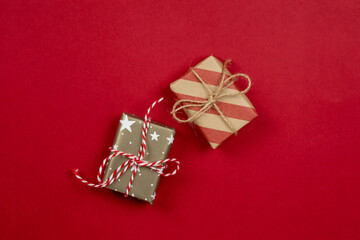 Two wrapped christmas presents and gift boxes wrapped in craft paper top view on red background...