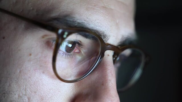 Tired and overworked young male with glasses looking at computer screen at night