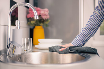 Hand of woman cleaning the kitchen counter and sink after washing dishes. Housewife doing housework concept. Closeup
