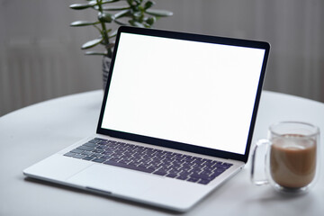 Fototapeta premium Close up laptop screen mockup on table with coffee cup and houseplant at home, no people